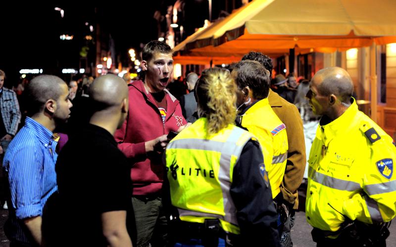 Agenten en groep mannen op straat, man is gewond