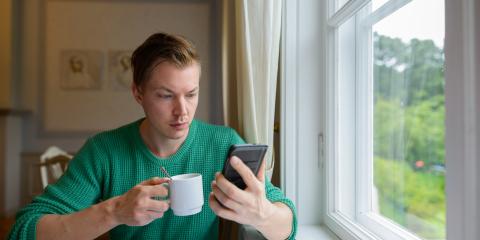 Jongeman zit aan tafel en heeft een kopje koffie en zijn telefoon vast