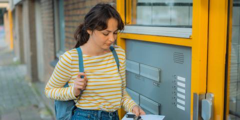 Jonge vrouw met een brief in haar handen, staat bij de brievenbus van een portiekflat 