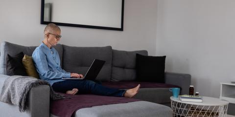 Een vrouw met kaalgeschoren hoofd zit op de bank en heeft een laptop op haar schoot