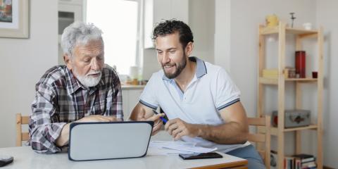 Man helpt senior man met het regelen van zaken. Ze kijken samen naar de papieren en een laptop.