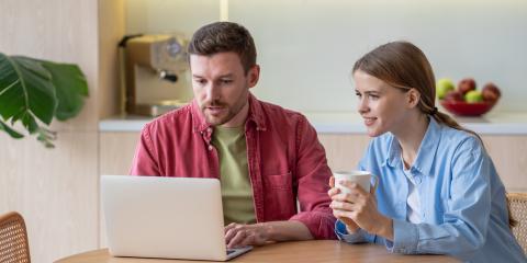 Een stel (man en vrouw) zitten samen aan de keukentafel en kijken naar een laptop