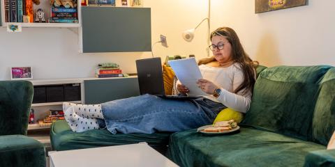 Jonge vrouw zit thuis op de bank en heeft papieren in haar hand