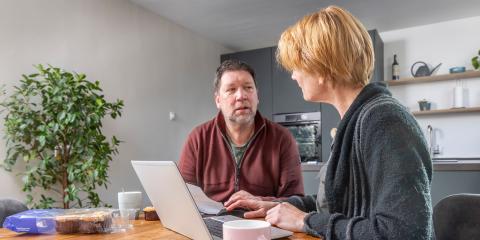 Man en vrouw thuis aan tafel met laptop en papieren voor zich.