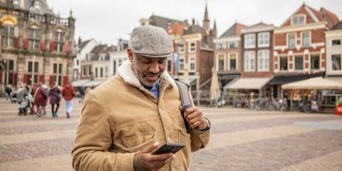 Een oudere man (55) staat op een plein in de binnenstad van Delft met een telefoon in zijn hand