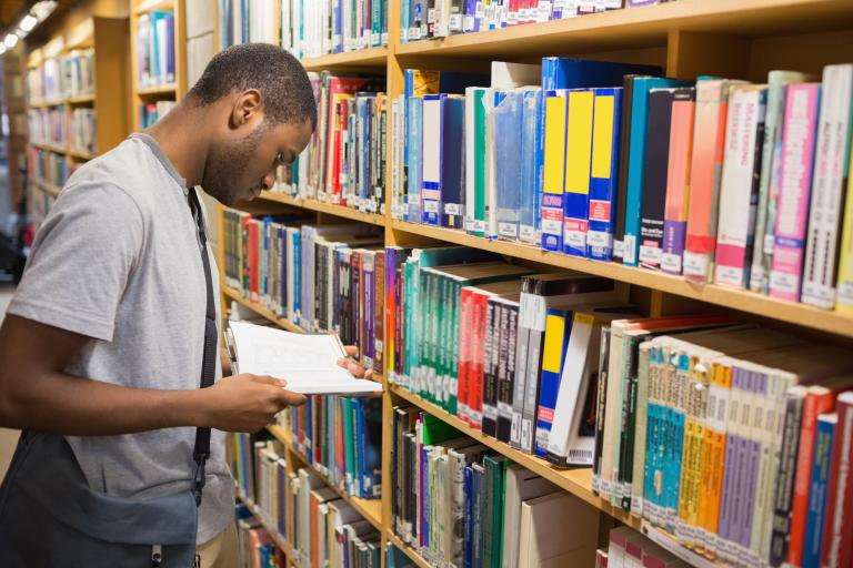 Student staat voor kast met boeken in bibliotheek